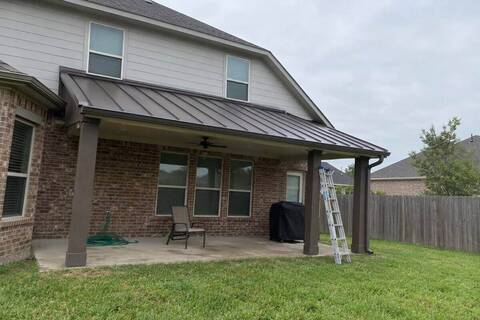 Dark bronze standing-seam metal roof over a backyard patio cover on a brick and siding house