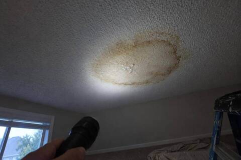 Brown water stain with a darker ring on a textured upstairs ceiling, lit by a flashlight