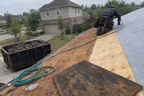 Roof tear-off in progress with bare plywood decking, a lighter replacement sheet, gray underlayment and a debris container below