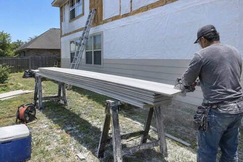 Primed fiber-cement planks on sawhorses beside a wall stripped to white house wrap