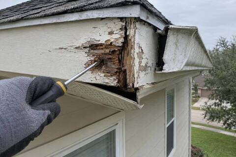 Screwdriver pushed into soft, split fascia at a roof corner with the gutter end pulled away